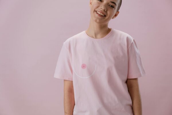 pexels-photo-5701647-5701647 Smiling person in pink shirt symbolizing breast cancer awareness with abstract design.